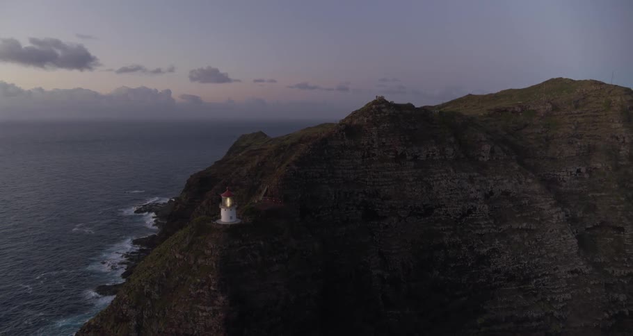 Lighthouse stands on promontory while waves crash against the shore