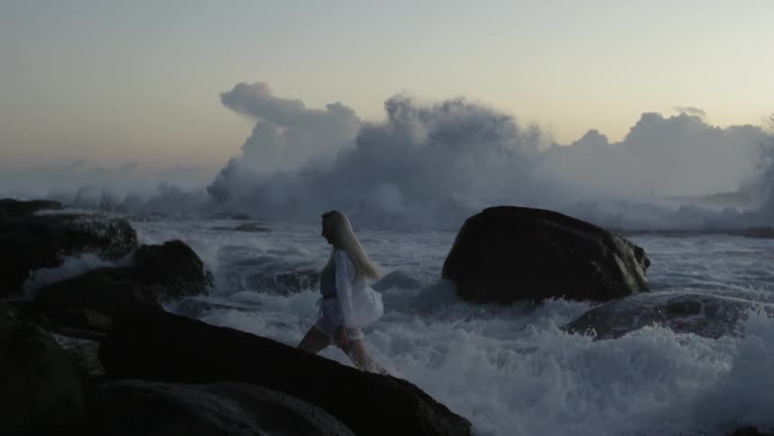 A woman in a white shirt walking along a rocky beach