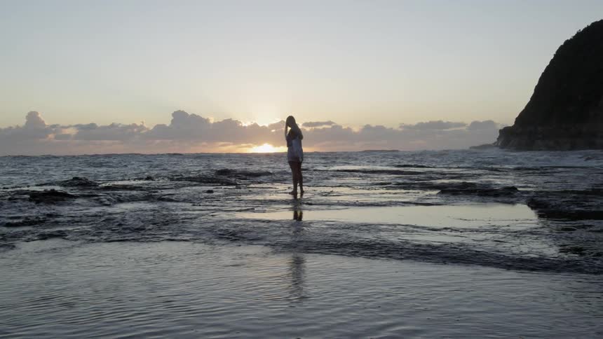 A young woman walks on a rocky shoreline and twirls