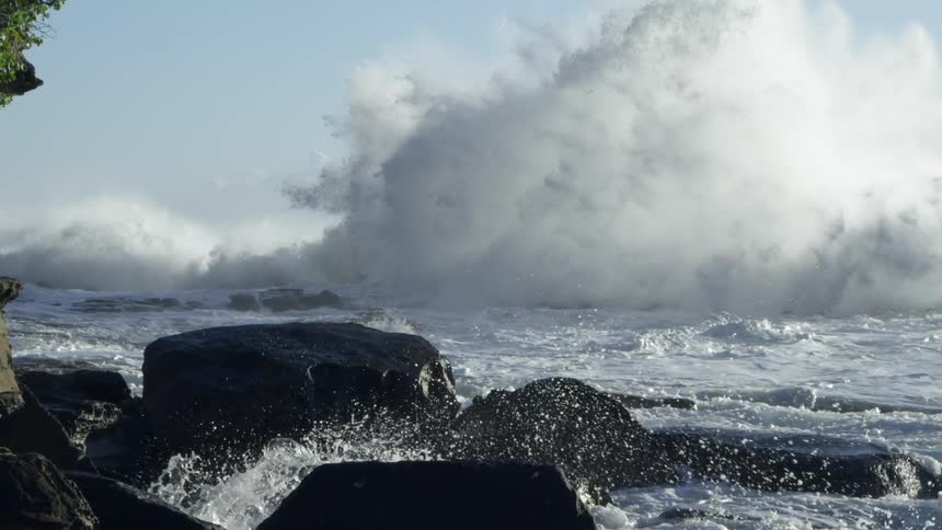 Massive waves rolling onto a rocky shore on a mostly clear day