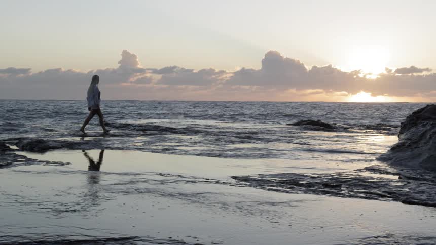 A woman walks in the water on a beach at dawn