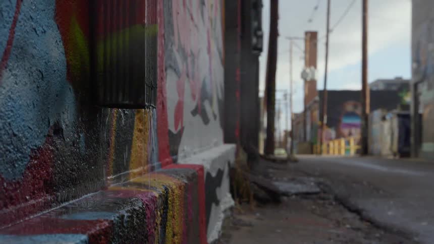 Water drips out of a gutter onto the side of a brightly painted building wall