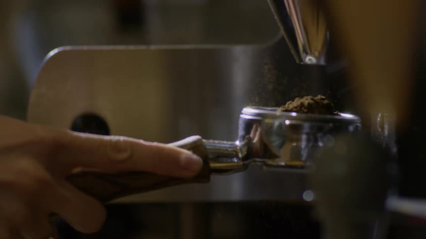 A person fills a filter holder with ground coffee to make espresso