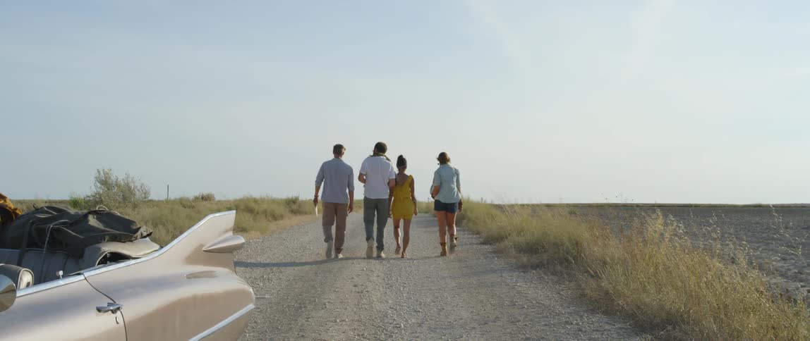 A family walking away from a retro car down a gravel road