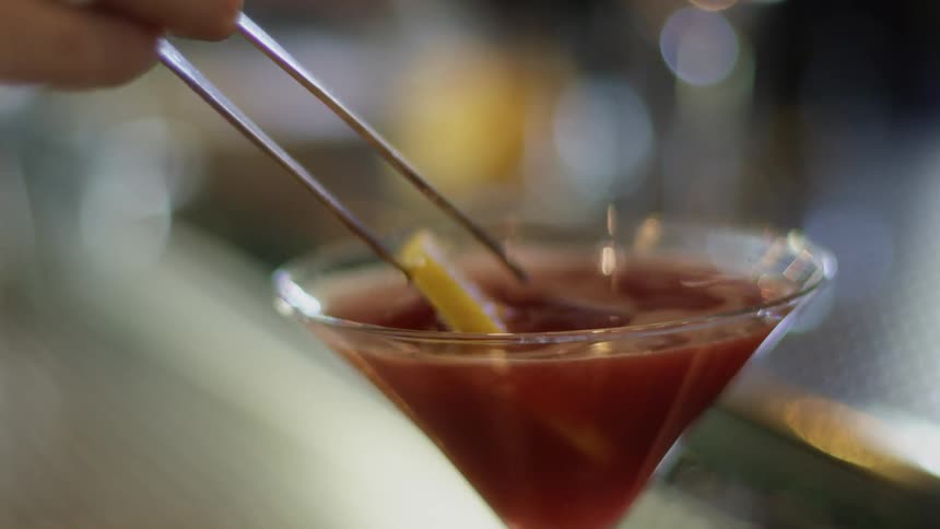 A bartender placing a lemon slice into a cocktail with steel tweezers