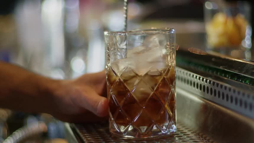 A bartender mixes a drink in glassware with a stirring spoon