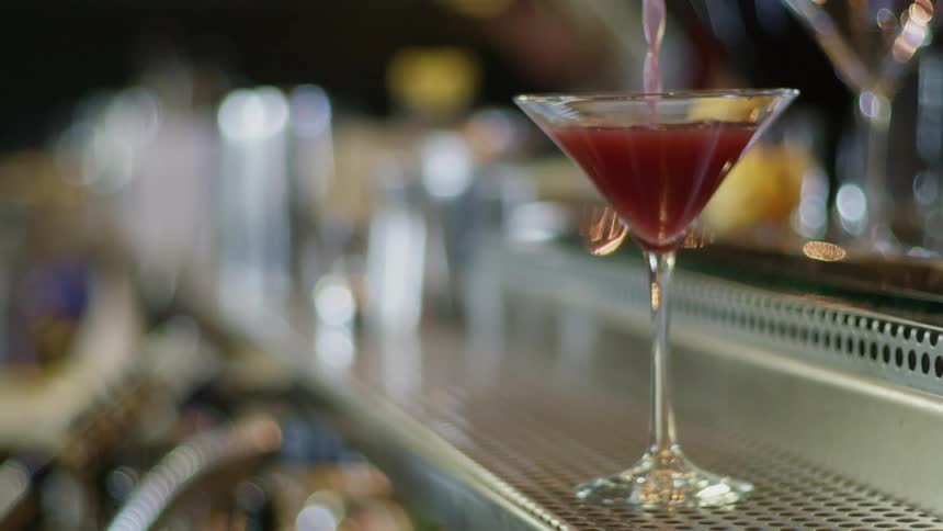 A red cocktail is poured in a martini glass