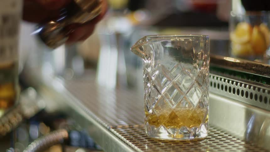 A bartender pours a shot into a mixing glass