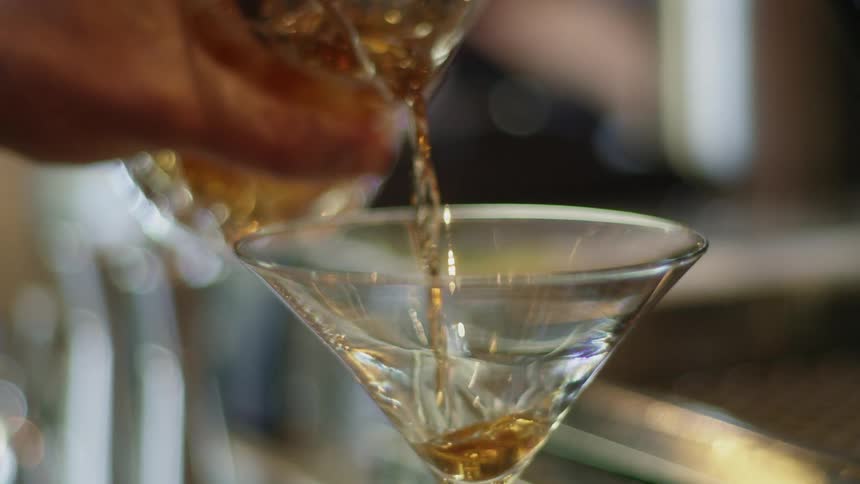 A bartender pours a cocktail into a martini glass