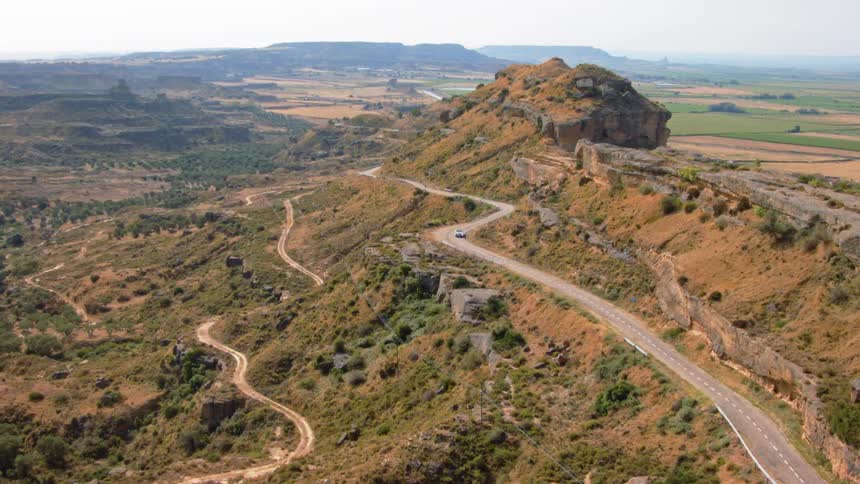 A vehicle drives along a winding road in the hills