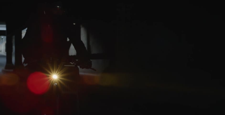 A motorcyclist rides through a dark tunnel under a bridge