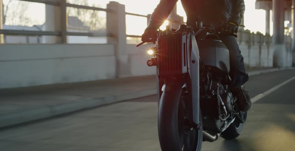 The sun shine glares as a motorcycle rider drives on an empty road under an overpass