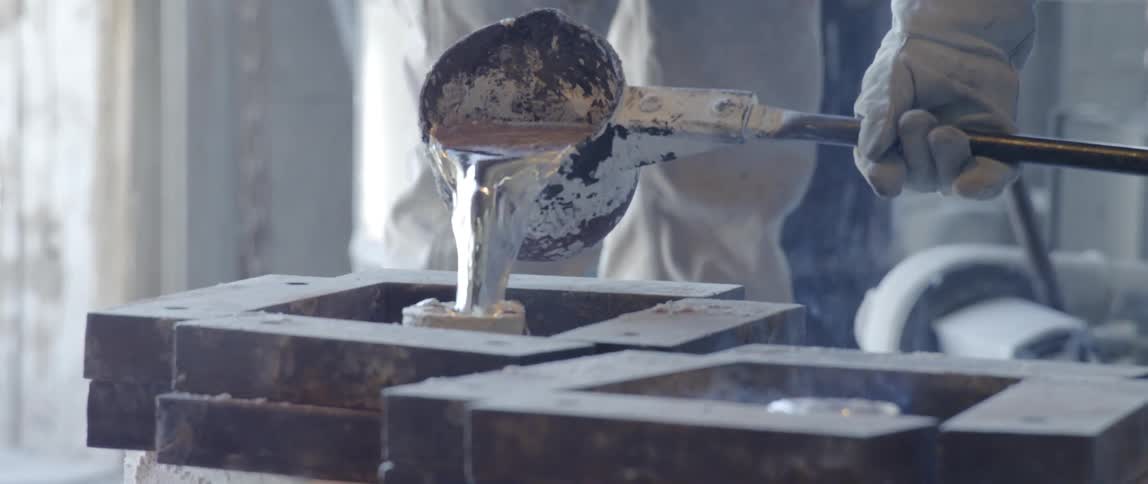 A person wearing heavy gloves pours molten metal into a tube form
