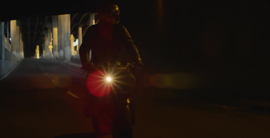 A man is riding his motorcycle under an overpass