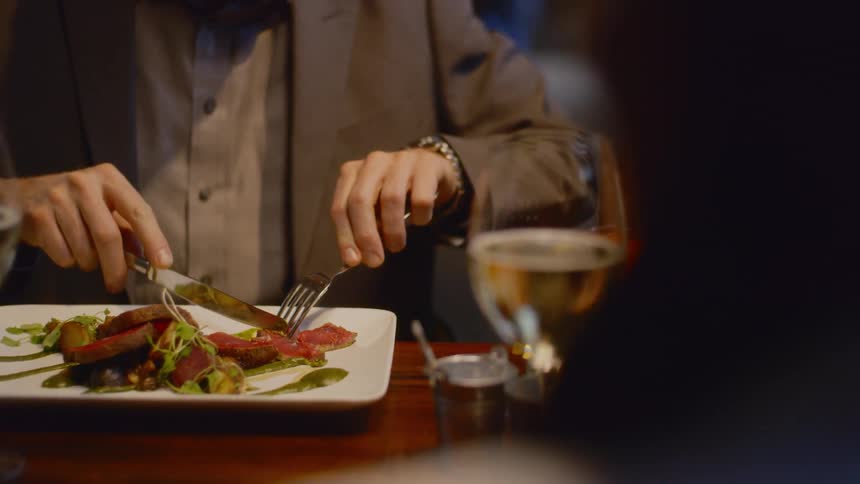 A man uses a knife and fork to cut his dinner at a restaurant