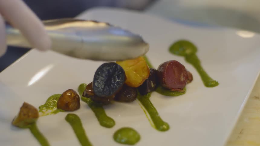 A chef places garnishes on a well decorated dinner plate
