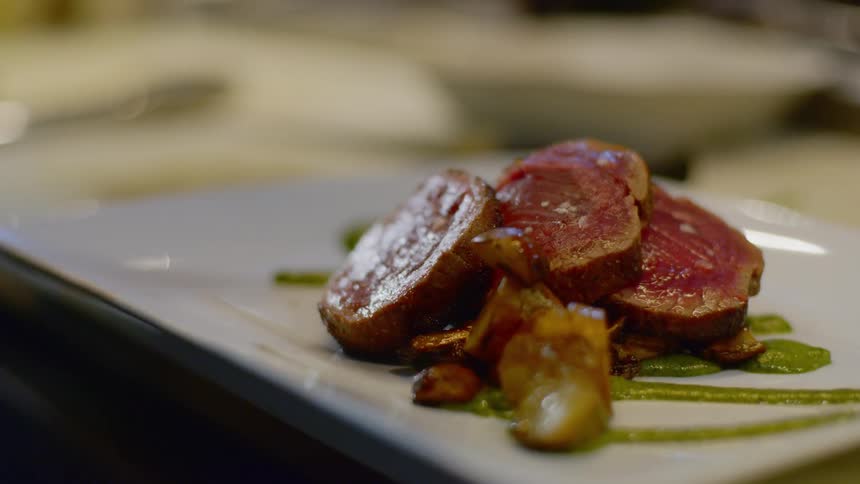 Lemon juice is squeezed onto vegetables beside medallions of rare meat before serving