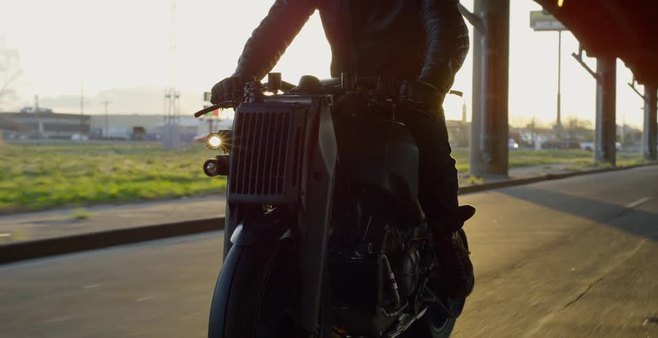 A man rides a motorcycle on a quiet highway under a bridge