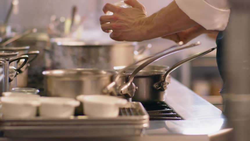 A chef scoops an ingredient out of a bowl and places it in a pot on the stove in a restaurant