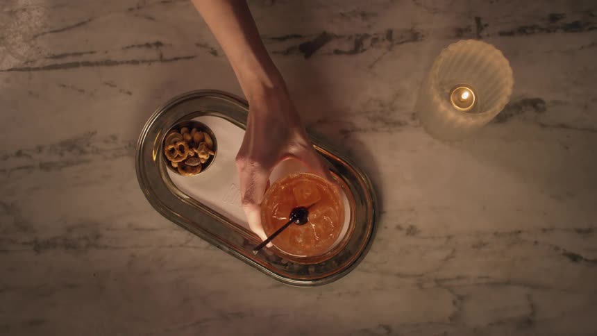 Caucasian woman placing a mixed drink on a serving tray that has a small container of assorted snack items on it
