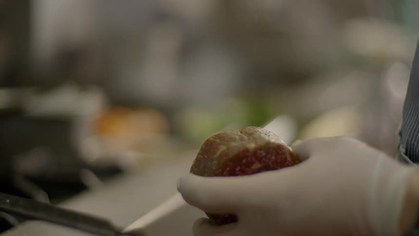 A man seasons a steak that hes holding while standing in front of a stove