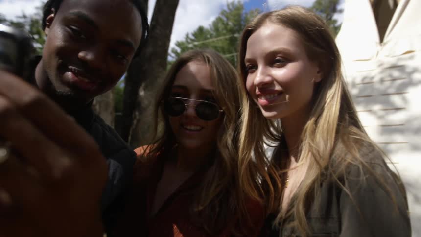 A young man takes a selfie of himself with two young women