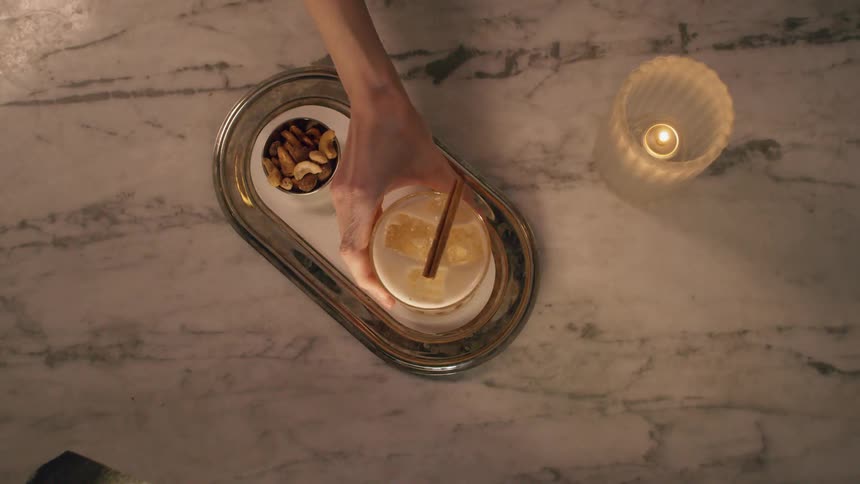 A person places a small glass of liquid and ice and a tray with nuts
