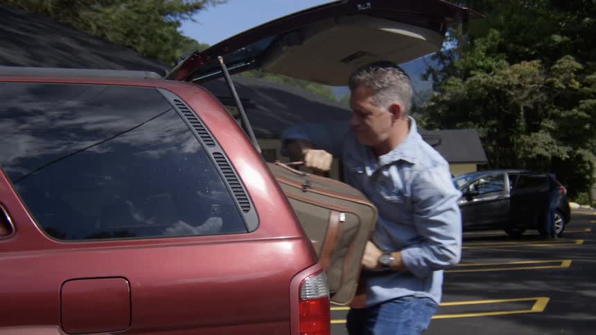 A man opens the back of an suv and removes a piece of luggage before closing it