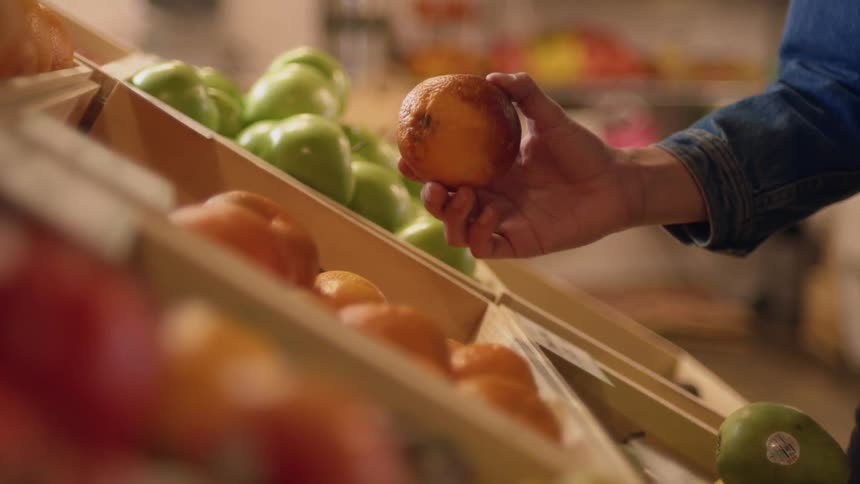 Male hand picking up an orange from fruit stand at a market