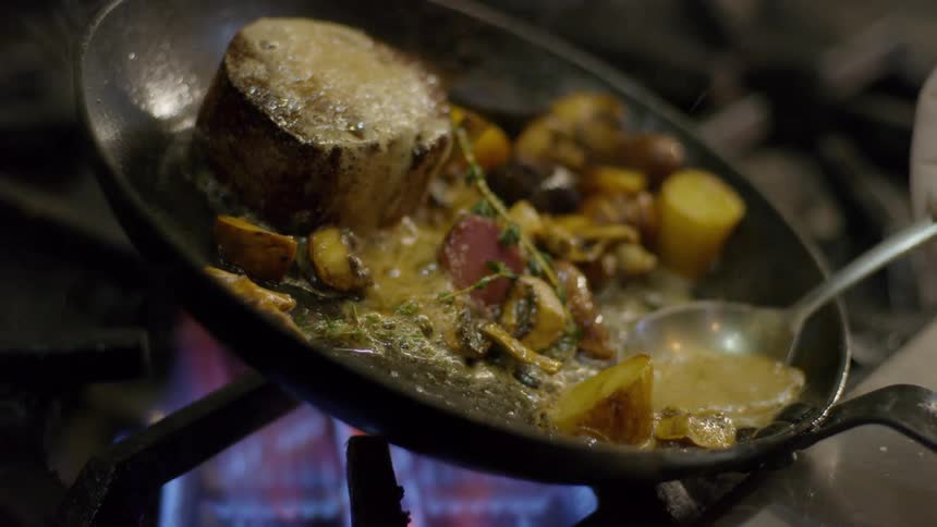 A cook ladles the fat over the food in the skillet