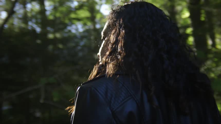 Woman walks through forest as sun shines through trees