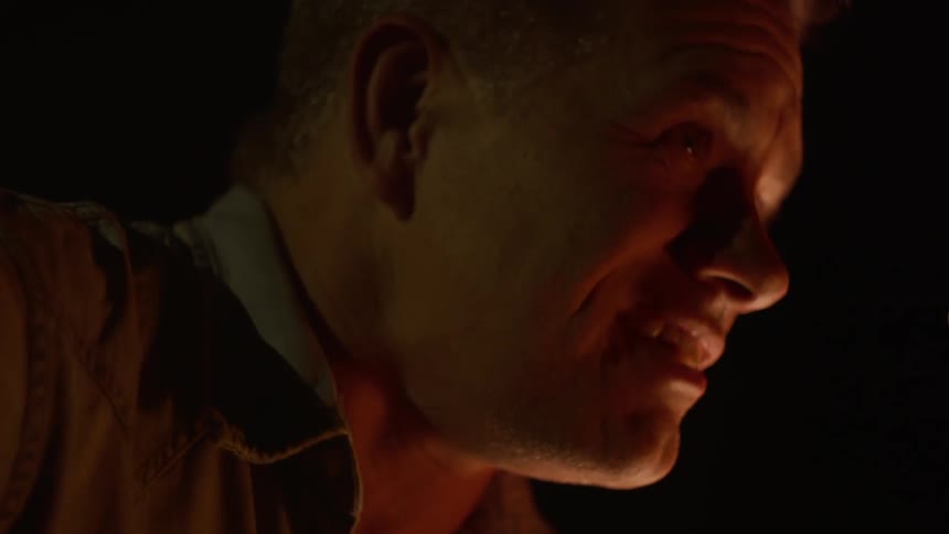 A white man sits outside in the dark and talks