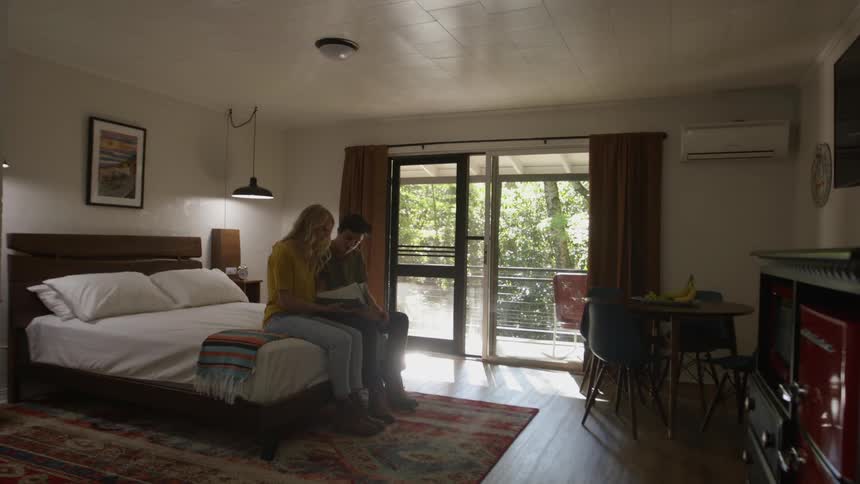 A man takes a seat next to a woman on the bed in a bedroom to look through a notebook
