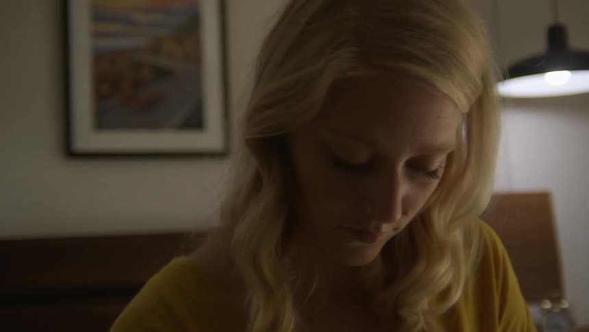 Blonde woman sitting on the bed looks down in the room
