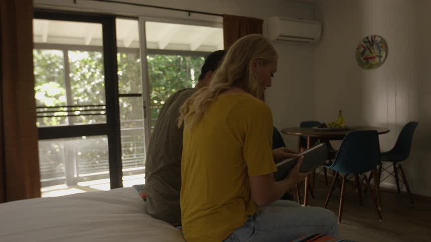 Man and woman are sitting on a bed together and looking at something