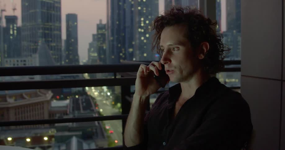 A man sitting near a window in a skyscraper talking on smartphone