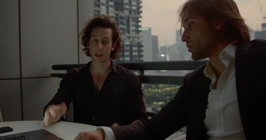 Two men sit at a desk and work on a laptop