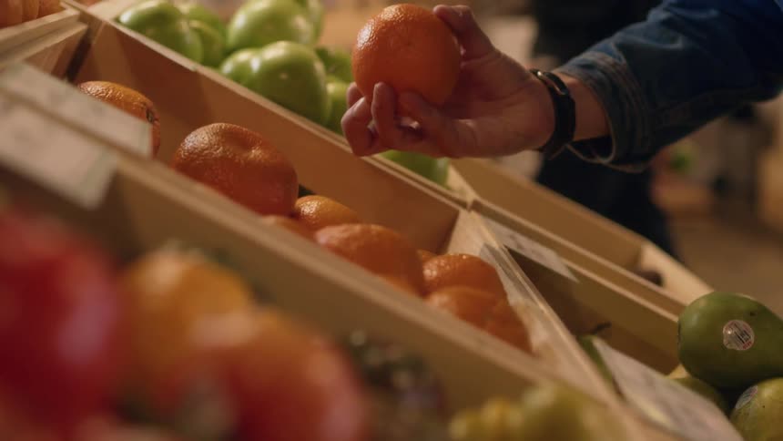 A woman walks toward produce and picks up an orange