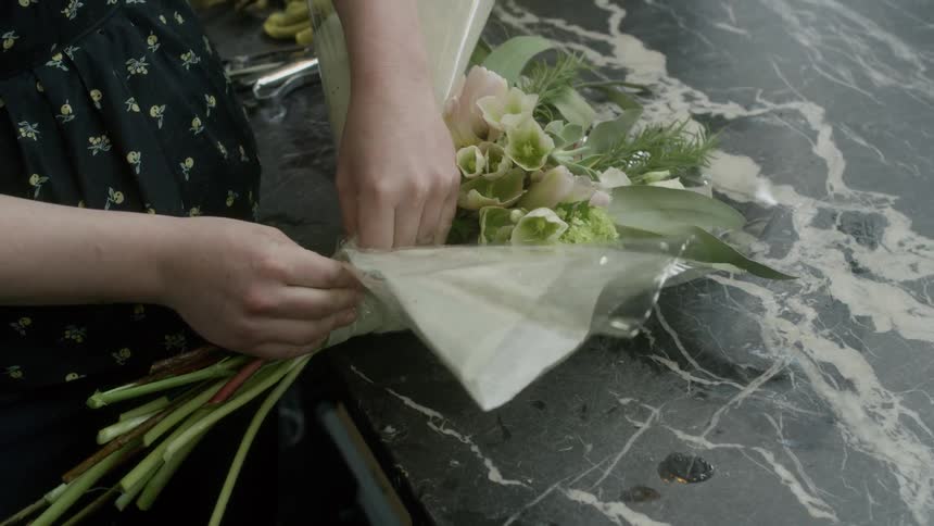A woman wraps a bouquet of flowers in paper