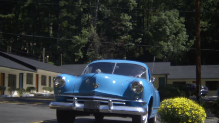 An old blue car pulls out of a parking lot