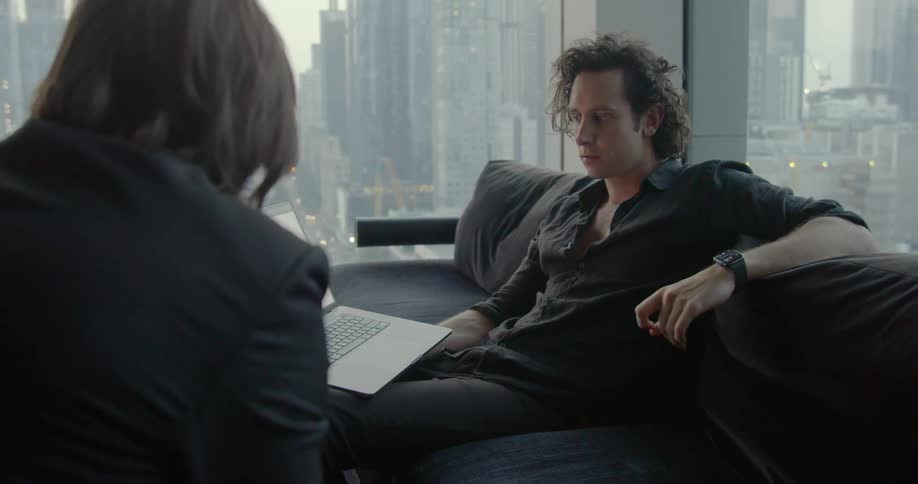 Two men talking about something on laptop while sitting in big city apartment
