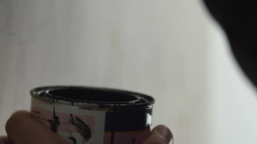 Person dipping a small paintbrush into a can of paint