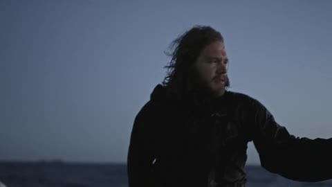 A bearded man riding a boat