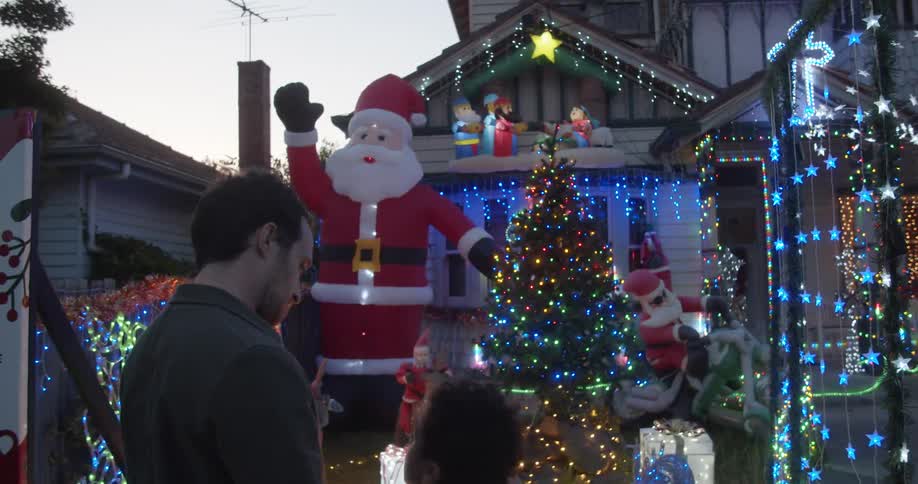 A boy points at a houses christmas light display and talks to his dad