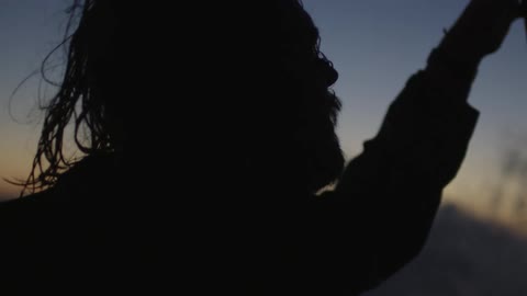 Silhouette of a bearded man sailing on rough seas at dusk