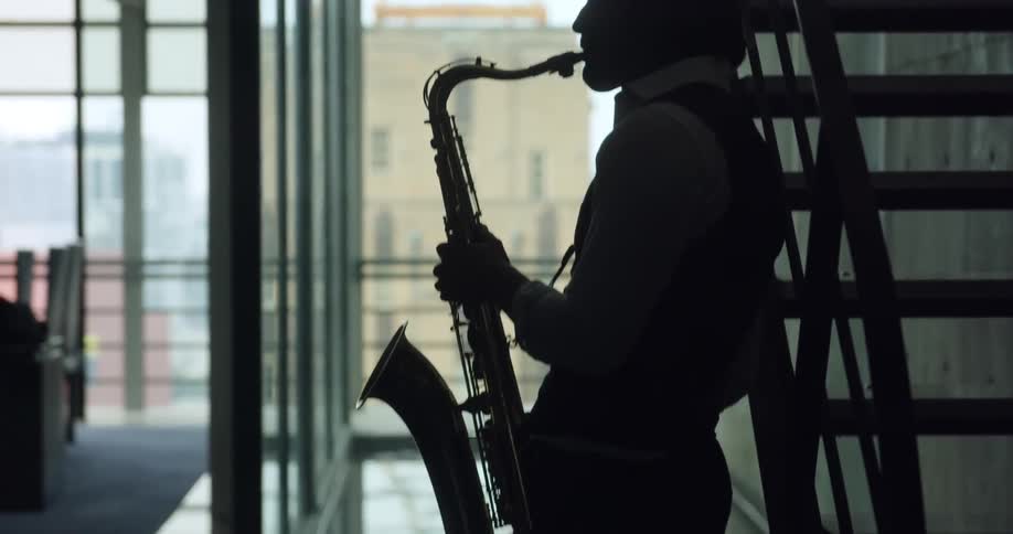 Male saxophonists silhouette plays saxophone next to the stairs in a room