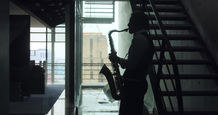 Male saxophonists silhouette plays saxophone next to the stairs in a room