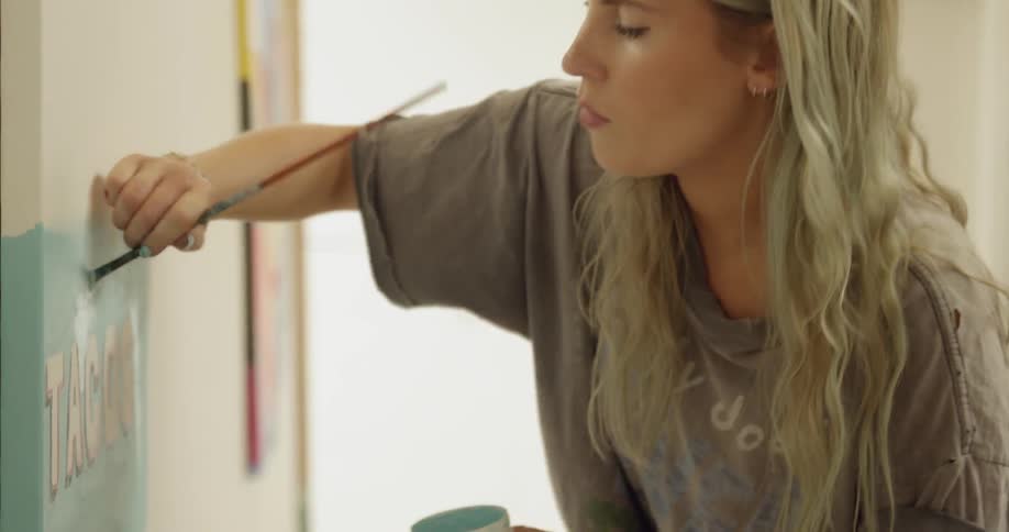 Woman with long blonde hair painting on a canvas indoors