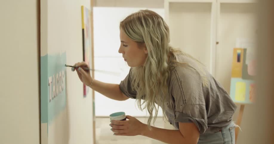 A woman paints on a canvas hanging on a wall