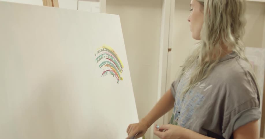 A female painter spreads a small patch of multicolored paint across the corner of her canvas